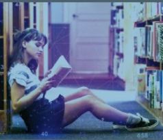 Niña sentada en el suelo de una biblioteca consultando un libro